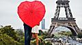 Couple visiting the Eiffel Tower standing with a red heart-shaped umbrella in Paris. Europe.